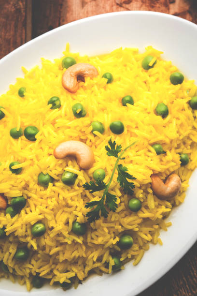 Basmati Rice Pilaf or pulav with Peas, or vegetable rice using green peas also known as matar pulav, with added yellow colour, served with plain dal